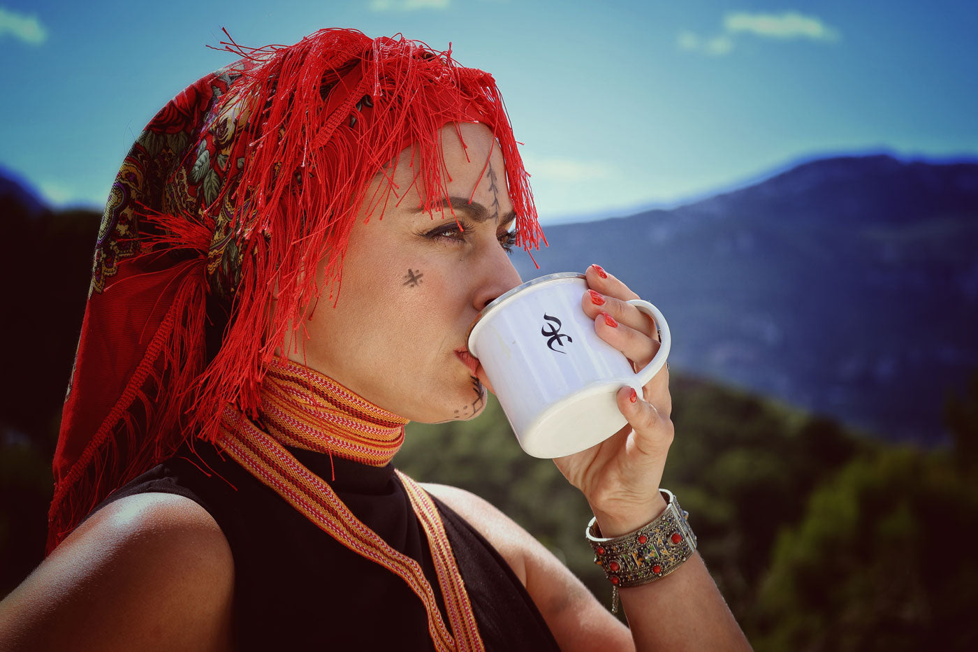 Femme kabyle berbère (amazighe) bois dans une tasse yaz par azamoul avec un amendil le foulard kabyle et dans un beau paysage de montagnes de kabylie