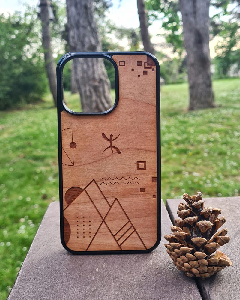 Coque en bois Abstract Amazigh l'univers amazigh berbère par Azamoul mode et accessoires berbères pour iPhone posée sur une table en nature forêt avec un pin