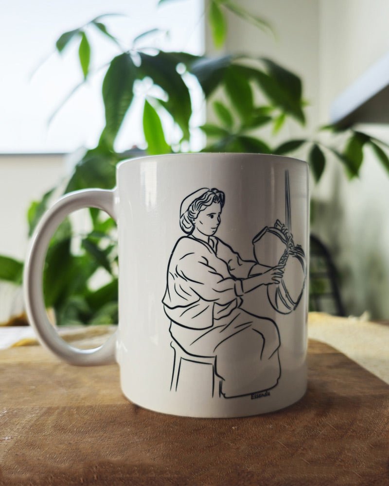 Un mug essendu la tradition kabyle berbère amazigh en céramique posé sur une table dans un salon, atmosphère chaleureuse avec une plante en arrière plan, tasse pour café ou thé fabriqué en france, azamoul mode et accessoires berberes amazigh et décoration intérieure