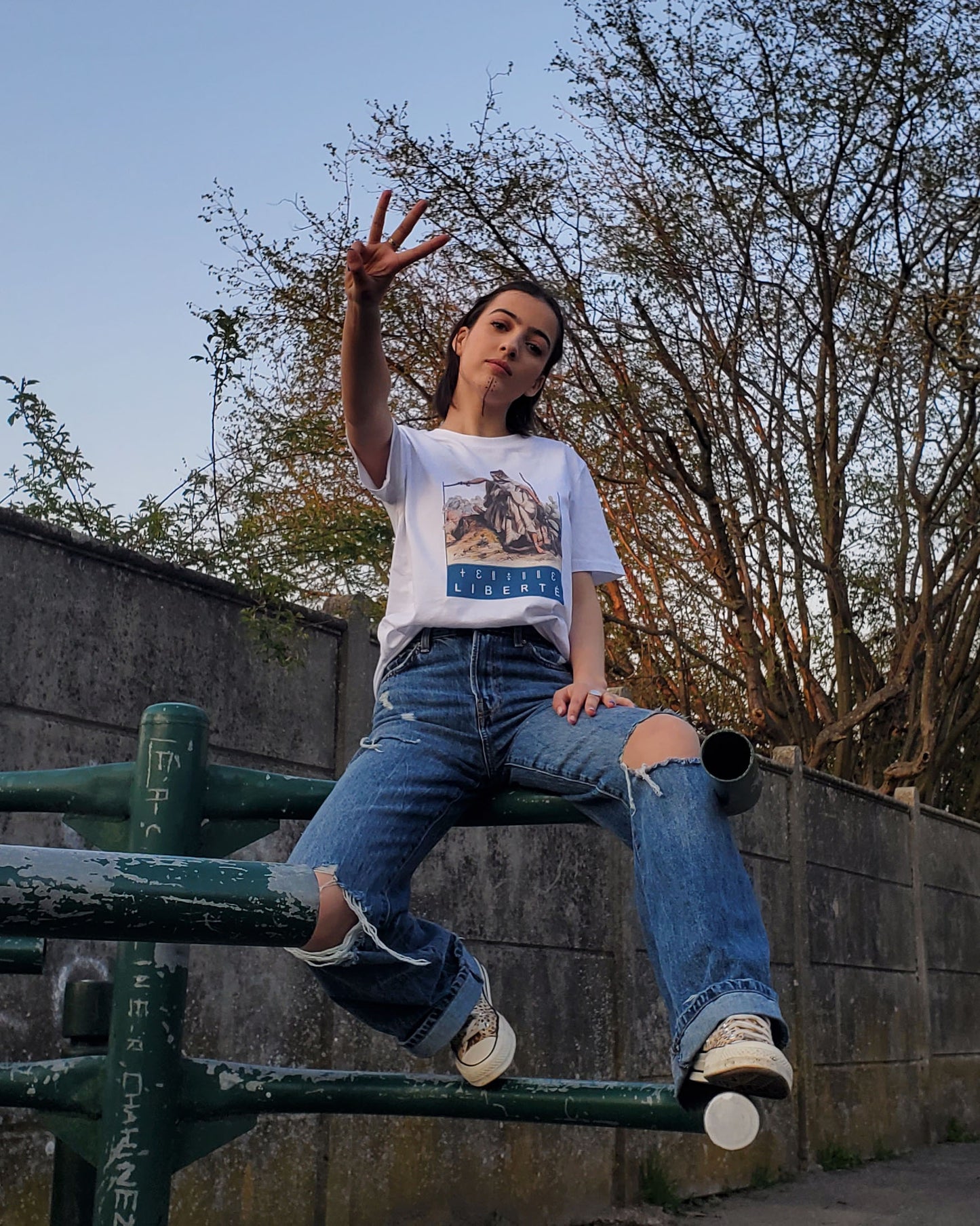 T-shirt Liberté Fatma Nsoumer porté par Taryel 2.0 dans un parc avec tatouages berbères et qui fait un geste de victoire - Azamoul mode et accessoires amazighs - Imprimé en France - 100% Coton Bio