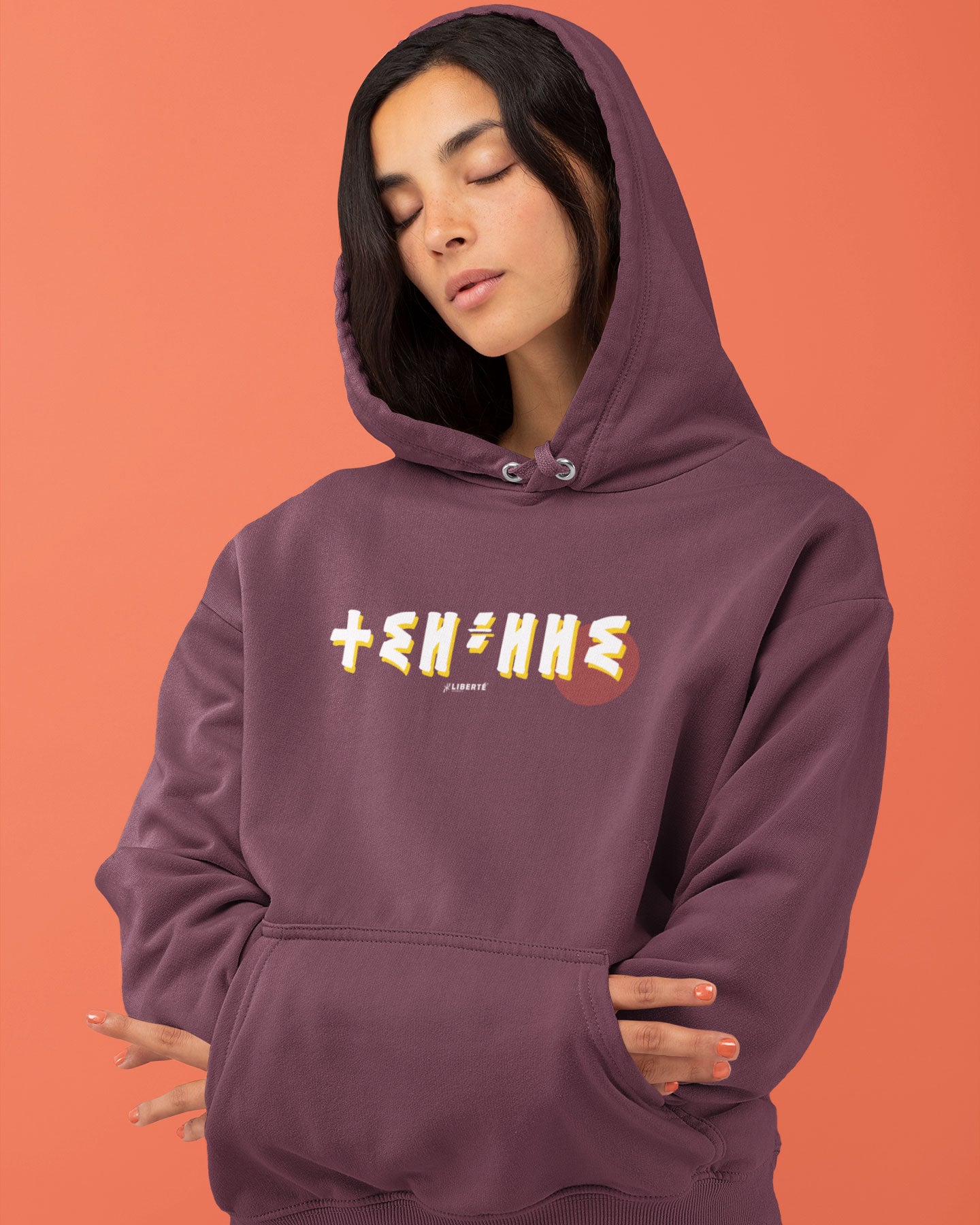 Femme qui porte un sweat à capuche thilelli liberte 100% coton bio, écrit en langue tifinagh, la langue des berbères amazigh par Azamoul mode et accessoires berbères,  de couleur bordeaux