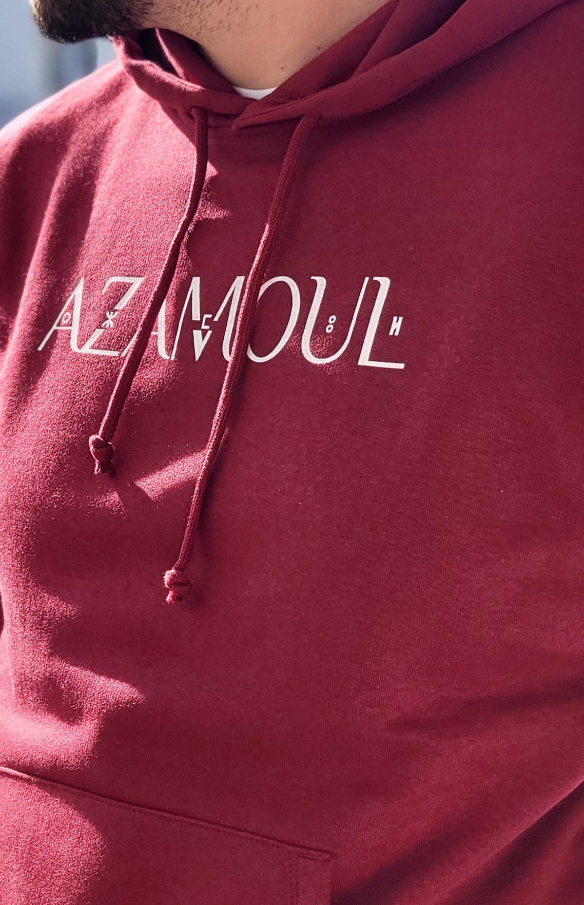Sweat à capuche Azamoul écriture supplémentaire en tifinagh langue berbère amazigh pour Homme  porté par un homme en plein soleil par azamoul mode et accessoires berbères couleur bordeaux