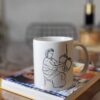 mug-essendou-made-in-franceazamoul-738813_3dd4a8ff-41d9-418e-9bcf-7f2391c6d6de Un mug en céramique essendu blanc posé sur un livre par azamoul mode et accessoires berbères amazigh, fabriqué en France
