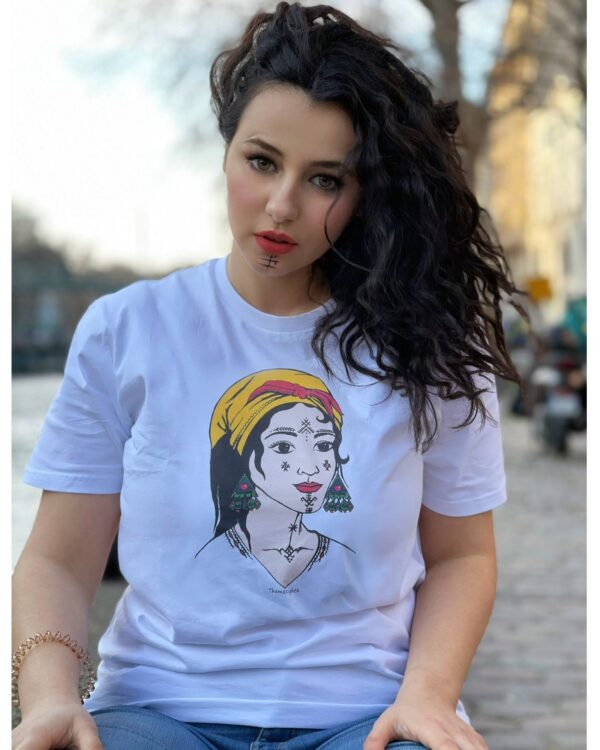 Alycia femme porte t-shirt femme berbère kabyle amazigh de azamoul blanc
T-shirt blanc femme berbère Amazigh par Azamoul Mode et Accessoires Berbères : design traditionnel avec tatouage facial symbolique, foulard kabyle amendil coloré, bijoux berbères et symbole berbère. Portez votre identité fièrement
