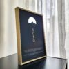 Une affiche murale de djurdjura écrite en alphabet tifinagh dans un cadre chic doré posée sur une table par azamoul mode accessoires berbères et décoration intérieure