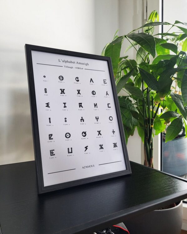 Affiche murale de l'alphabet berbère, Tifinagh, de couleur noire posée sur un bureau à coté d'une fleur dans un cadre de décoration intérieure par Azamoul mode et accessoires berbères amazigh