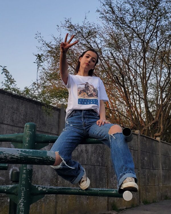 T-shirt Liberté Fatma Nsoumer porté par Taryel 2.0 dans un parc avec tatouages berbères et qui fait un geste de victoire - Azamoul mode et accessoires amazighs - Imprimé en France - 100% Coton Bio
